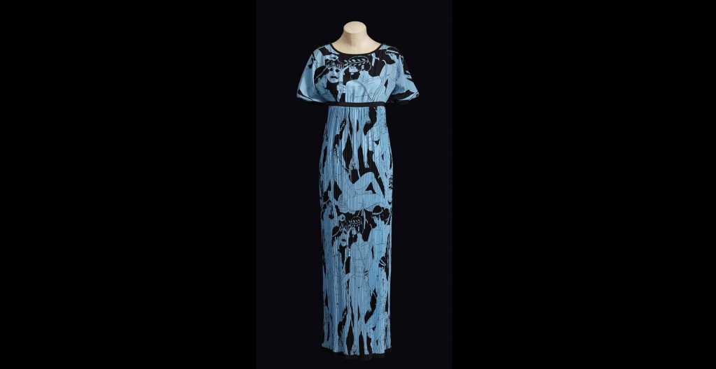 Evening-gown. Spring-Summer 1971 haute couture collection. Blue and black printed crepe de chine with pattern of ancient Greek figures; short sleeved bodice with empire waist emphasized by black silk crepe bias tape; skirt with sunburst pleating. © Fondation Pierre Bergé–Yves Saint Laurent, Paris. Photo Sophie Carre